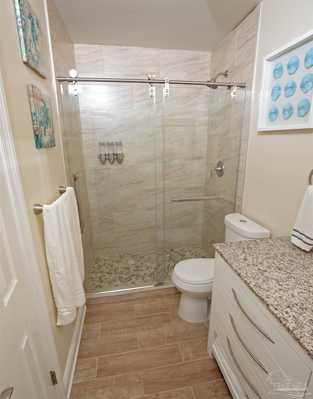 bathroom featuring vanity, wood finished floors, toilet, and a shower stall