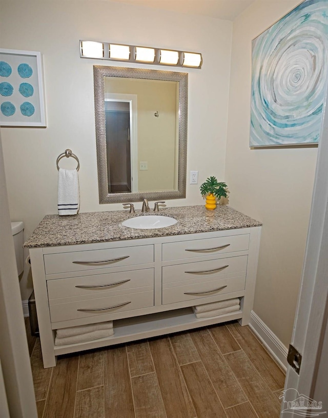 bathroom with toilet, baseboards, wood finished floors, and vanity