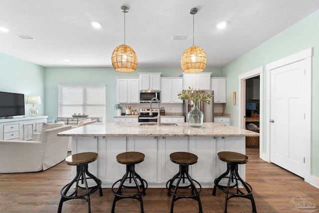 kitchen with white cabinetry, light stone counters, stainless steel appliances, and decorative light fixtures