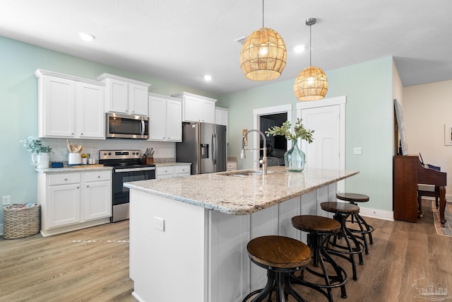 kitchen featuring sink, white cabinetry, stainless steel appliances, decorative light fixtures, and a kitchen island with sink