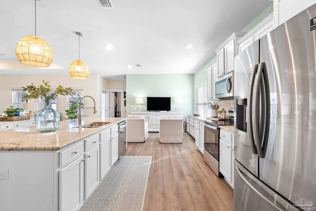 kitchen with white cabinets, hanging light fixtures, a kitchen island with sink, sink, and stainless steel appliances