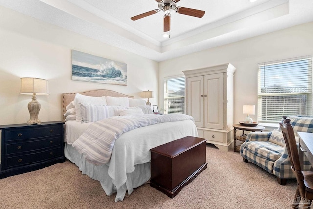 bedroom with ceiling fan, light colored carpet, and a raised ceiling