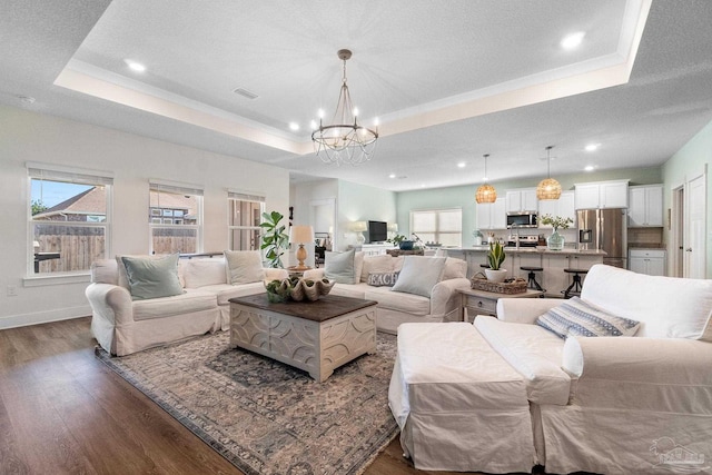 living room featuring dark hardwood / wood-style flooring, an inviting chandelier, a textured ceiling, and a raised ceiling