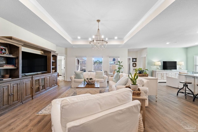 living room with an inviting chandelier, a tray ceiling, and light hardwood / wood-style floors