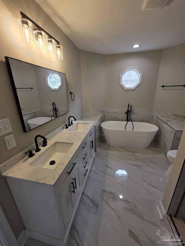 5674 Windsong Dr, Milton, FL 32570 - bathroom with marble look tiles, a textured ceiling, a freestanding bath, double vanity, and tile walls