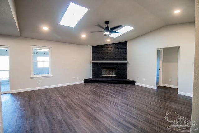 unfurnished living room featuring dark hardwood / wood-style flooring, ceiling fan, vaulted ceiling with skylight, and a brick fireplace