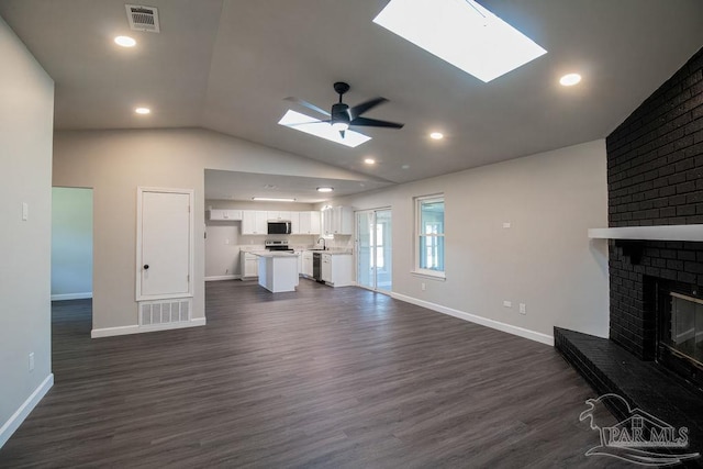 unfurnished living room featuring ceiling fan, sink, dark wood-type flooring, a brick fireplace, and vaulted ceiling with skylight