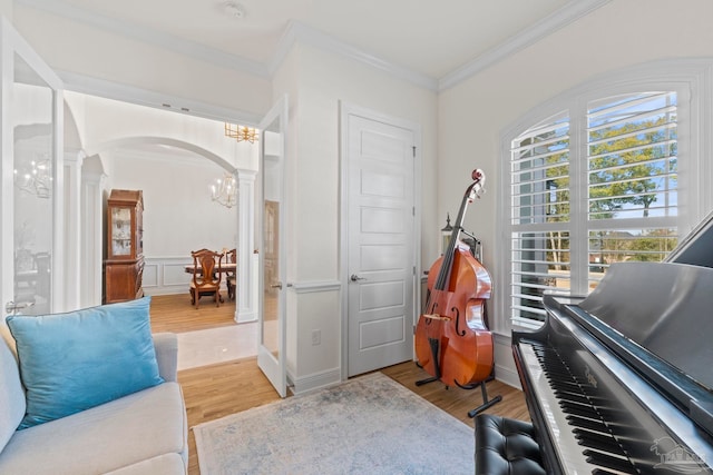 sitting room featuring arched walkways, ornamental molding, decorative columns, and light wood-style floors