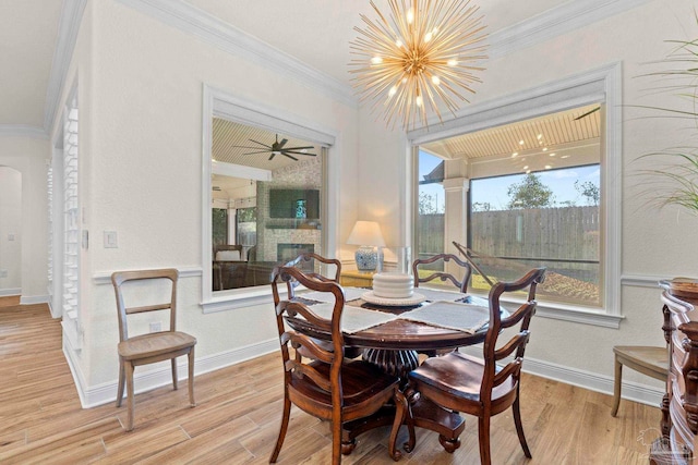 dining space featuring arched walkways, a stone fireplace, ornamental molding, light wood finished floors, and an inviting chandelier