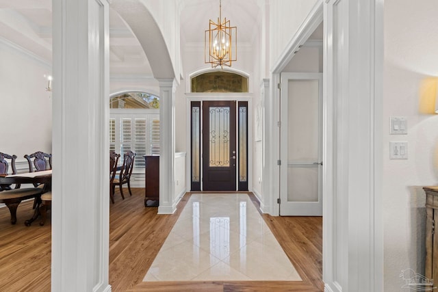 foyer featuring decorative columns, baseboards, light wood-style flooring, ornamental molding, and a notable chandelier