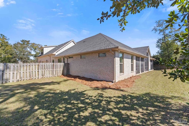 view of home's exterior with roof with shingles, brick siding, a lawn, and fence