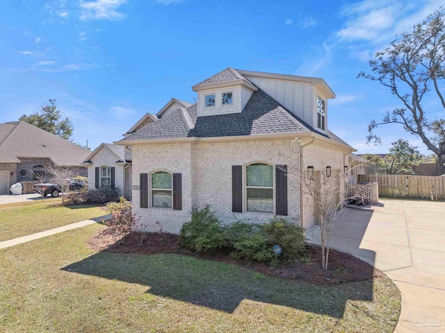 view of front of house featuring brick siding, roof with shingles, concrete driveway, fence, and a front lawn