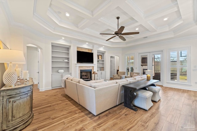 living room with arched walkways, ornamental molding, light wood-type flooring, and a fireplace