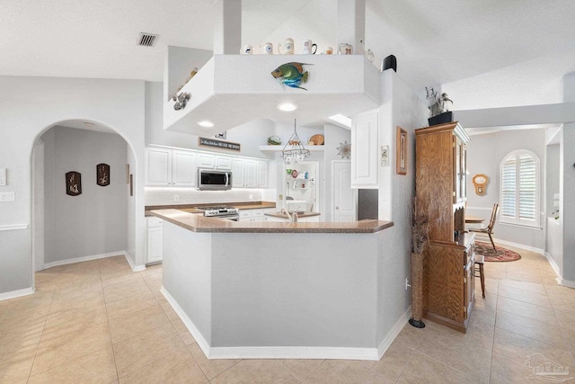 kitchen featuring light tile patterned floors, stainless steel appliances, white cabinets, vaulted ceiling, and kitchen peninsula