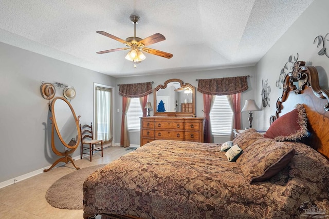 tiled bedroom featuring a raised ceiling, a textured ceiling, and ceiling fan