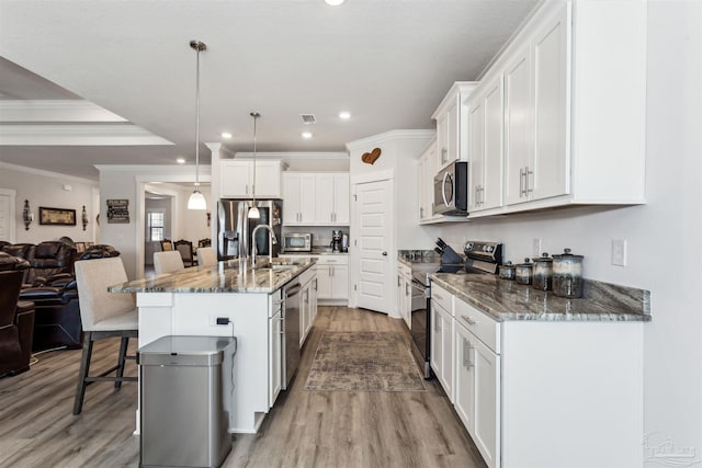 kitchen with a kitchen island with sink, appliances with stainless steel finishes, white cabinets, and decorative light fixtures