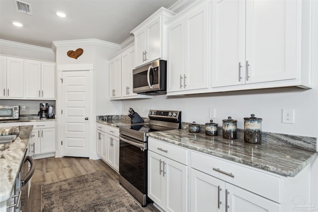 kitchen with visible vents, appliances with stainless steel finishes, ornamental molding, white cabinets, and light stone countertops