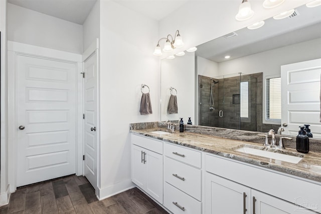 bathroom featuring double vanity, a shower stall, a sink, and wood finished floors