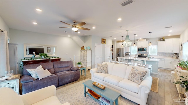 living room with ceiling fan with notable chandelier, sink, and light hardwood / wood-style flooring