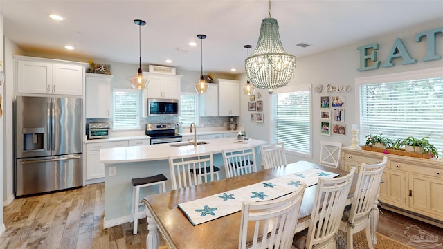 kitchen with decorative light fixtures, decorative backsplash, sink, appliances with stainless steel finishes, and an island with sink