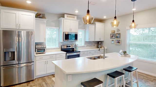 kitchen featuring appliances with stainless steel finishes, white cabinetry, sink, hanging light fixtures, and backsplash