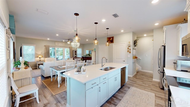 kitchen with sink, white cabinetry, hanging light fixtures, appliances with stainless steel finishes, and an island with sink