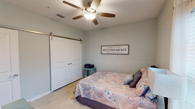 bedroom featuring light carpet, ceiling fan, a closet, and a barn door