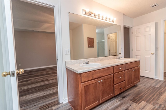 bathroom with wood finished floors, baseboards, double vanity, and an enclosed shower