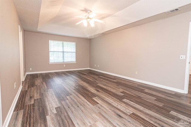 spare room with a raised ceiling, ceiling fan, dark wood-type flooring, and baseboards