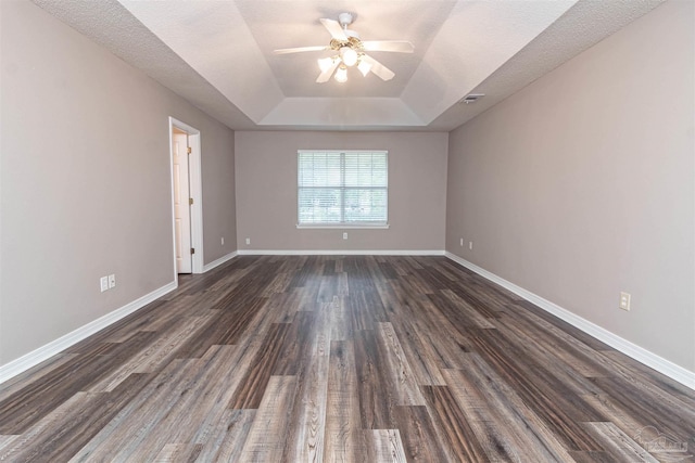 unfurnished room with a tray ceiling, ceiling fan, dark wood-style flooring, and baseboards