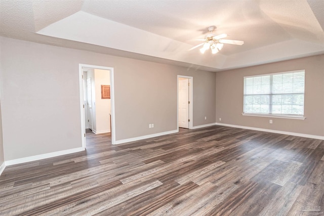 unfurnished room with a raised ceiling, dark wood-style floors, ceiling fan, baseboards, and a textured ceiling