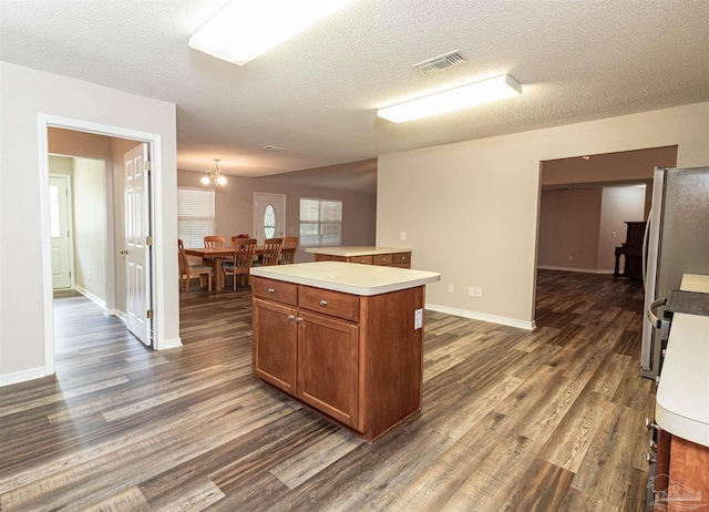 kitchen featuring dark wood-style floors, brown cabinetry, light countertops, a center island, and a textured ceiling
