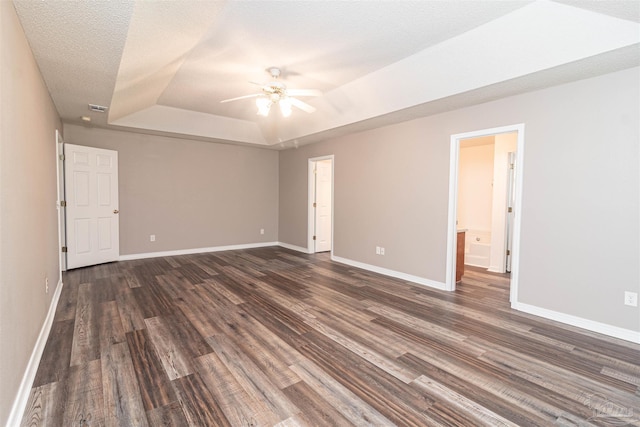 unfurnished bedroom with a tray ceiling, dark wood-style flooring, and baseboards