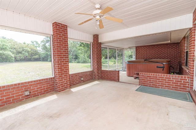 unfurnished sunroom with a jacuzzi, a ceiling fan, and brick wall