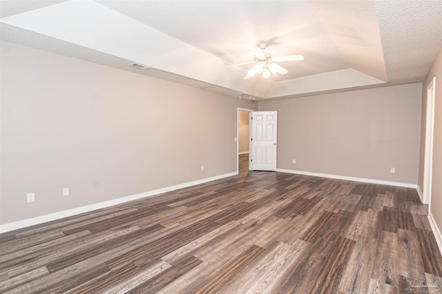 unfurnished room with a tray ceiling, ceiling fan, dark wood-style flooring, and baseboards