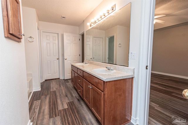full bathroom featuring wood finished floors, baseboards, double vanity, a ceiling fan, and a textured ceiling