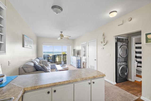 kitchen featuring white cabinets, dark hardwood / wood-style flooring, stacked washing maching and dryer, and ceiling fan