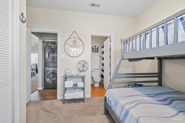 carpeted bedroom with ensuite bathroom and stacked washer and clothes dryer