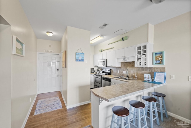 kitchen with sink, stainless steel appliances, kitchen peninsula, hardwood / wood-style floors, and white cabinets