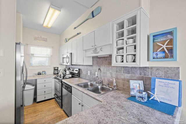 kitchen with appliances with stainless steel finishes, light wood-type flooring, tasteful backsplash, sink, and white cabinetry