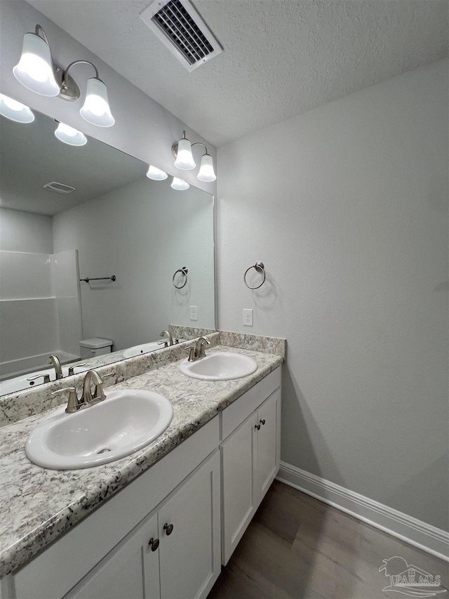 bathroom with hardwood / wood-style flooring, vanity, a textured ceiling, toilet, and walk in shower