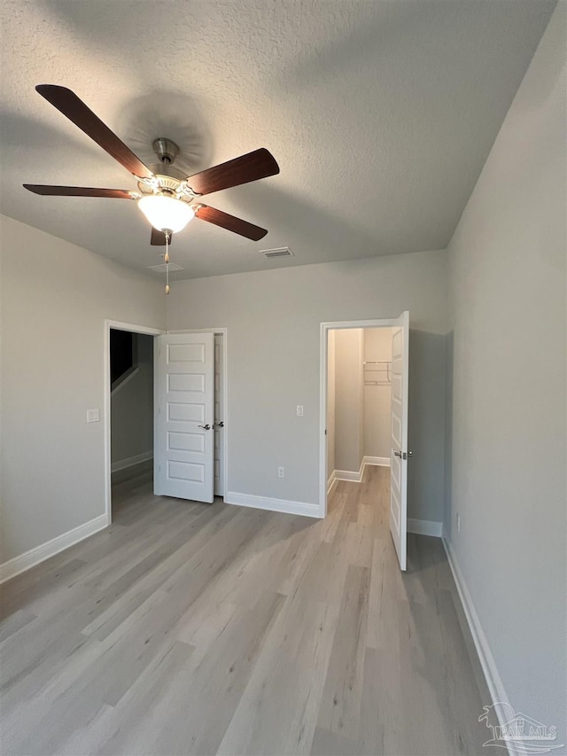 unfurnished bedroom featuring a spacious closet, a textured ceiling, a closet, and light hardwood / wood-style flooring