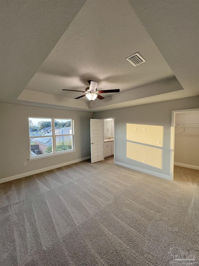 unfurnished bedroom with a walk in closet, light colored carpet, ceiling fan, a raised ceiling, and a textured ceiling