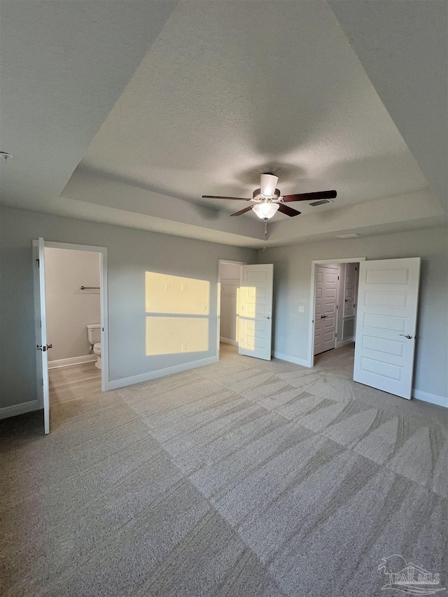 unfurnished bedroom featuring light colored carpet, ensuite bathroom, a raised ceiling, and a textured ceiling