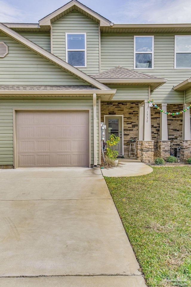 multi unit property featuring an attached garage, driveway, stone siding, and a front yard