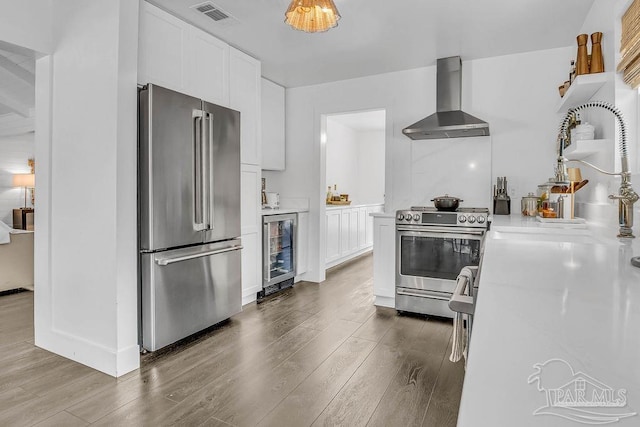 6050 Cheyenne Dr, Milton, FL 32570 - kitchen featuring appliances with stainless steel finishes, wall chimney exhaust hood, wine cooler, dark wood-style flooring, and white cabinets