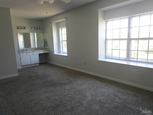 interior space featuring dark colored carpet, ceiling fan, plenty of natural light, and a textured ceiling