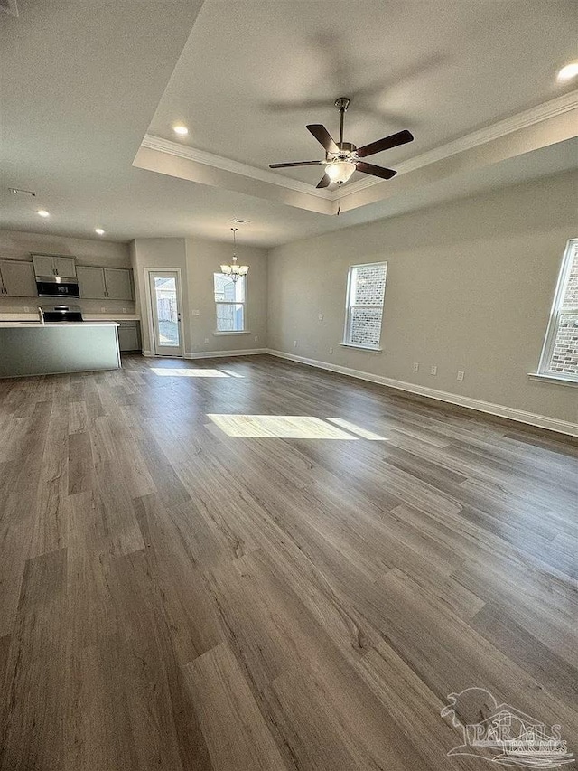1636 Slate Dr, Cantonment, FL 32533 - unfurnished living room featuring a raised ceiling, baseboards, a chandelier, dark wood finished floors, and a ceiling fan