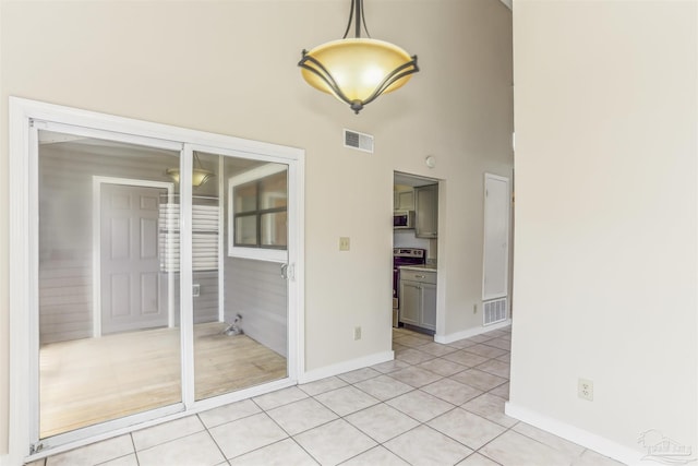 interior space with visible vents, baseboards, a towering ceiling, and light tile patterned floors