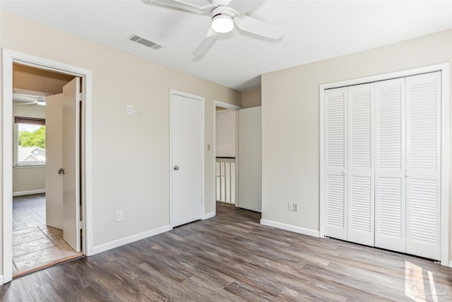 unfurnished bedroom with ceiling fan, visible vents, wood finished floors, baseboards, and a closet